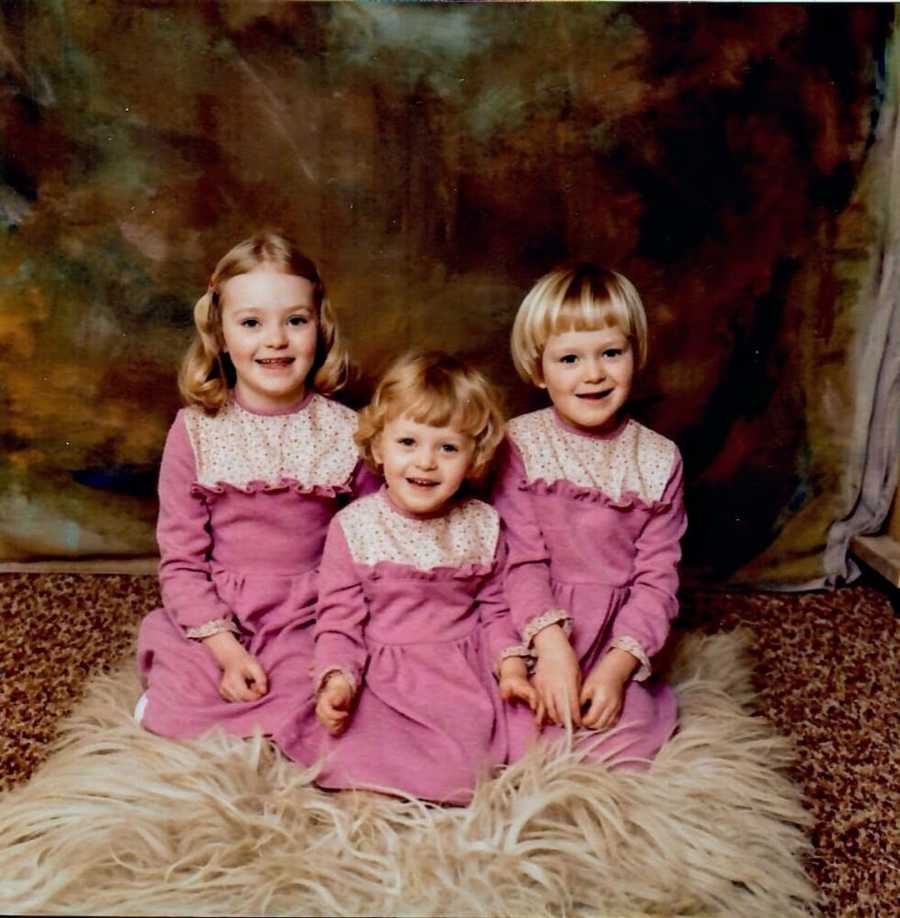 Three blonde sisters wearing pink dresses kneeling on floor