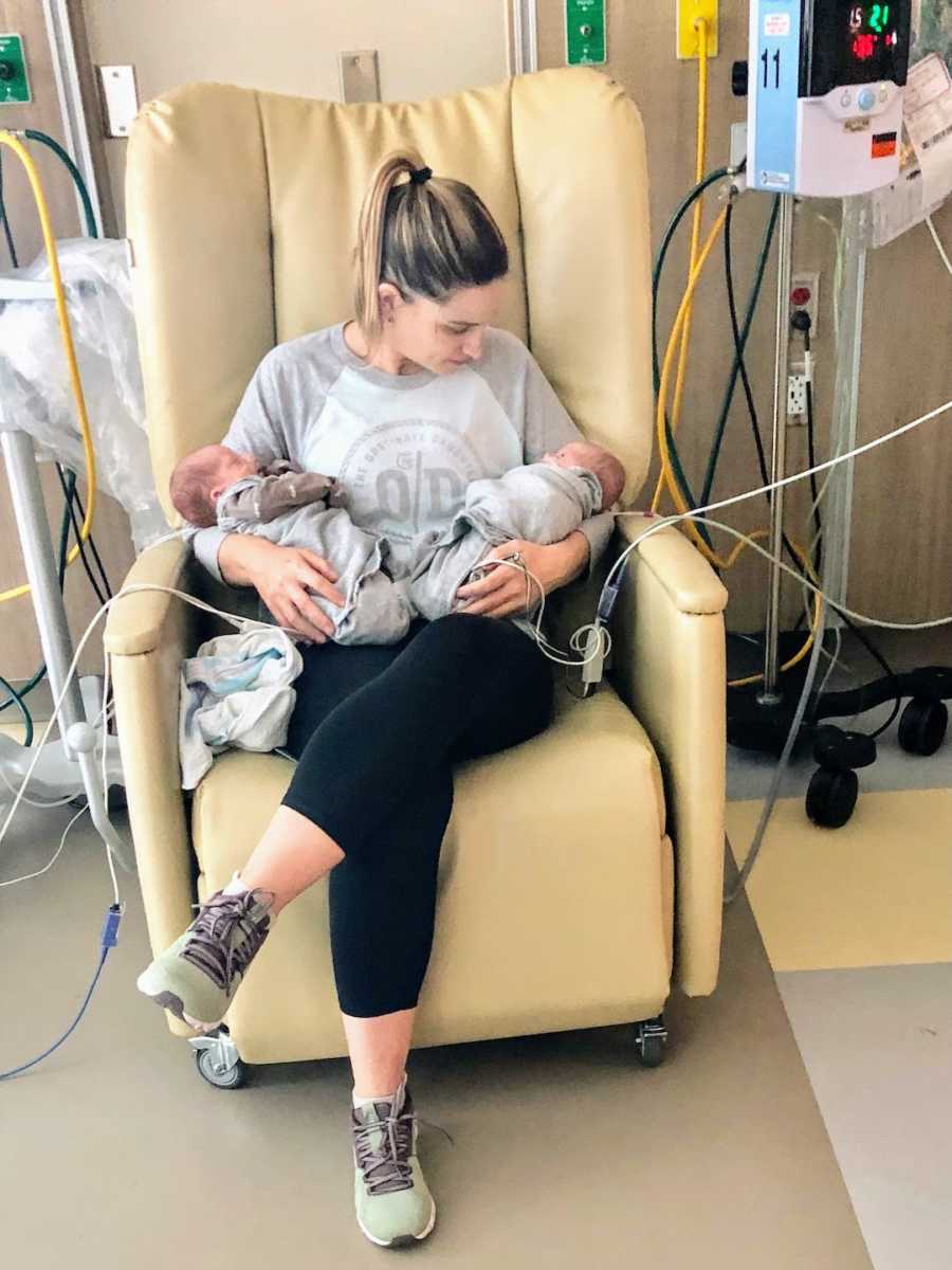 New mom sitting in chair holding newborn twin boys in hospital