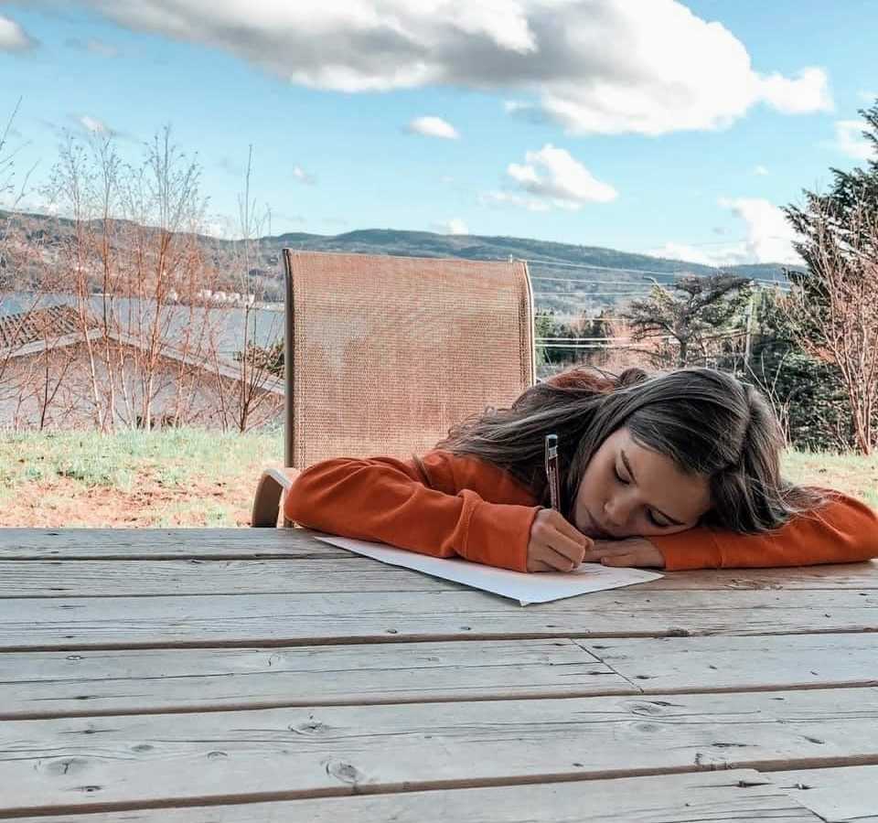 A girl rests her head on an outdoor table while writing