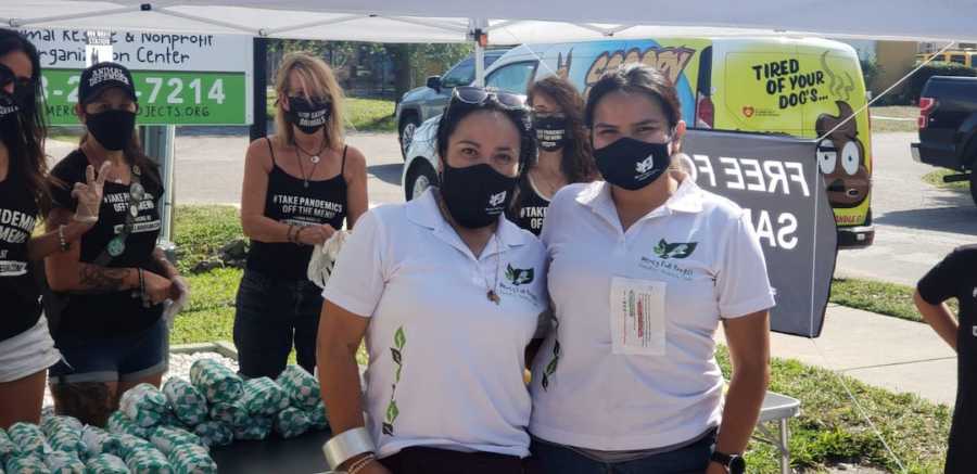 Two girls wearing matching white shirts with masks on, volunteers in the back