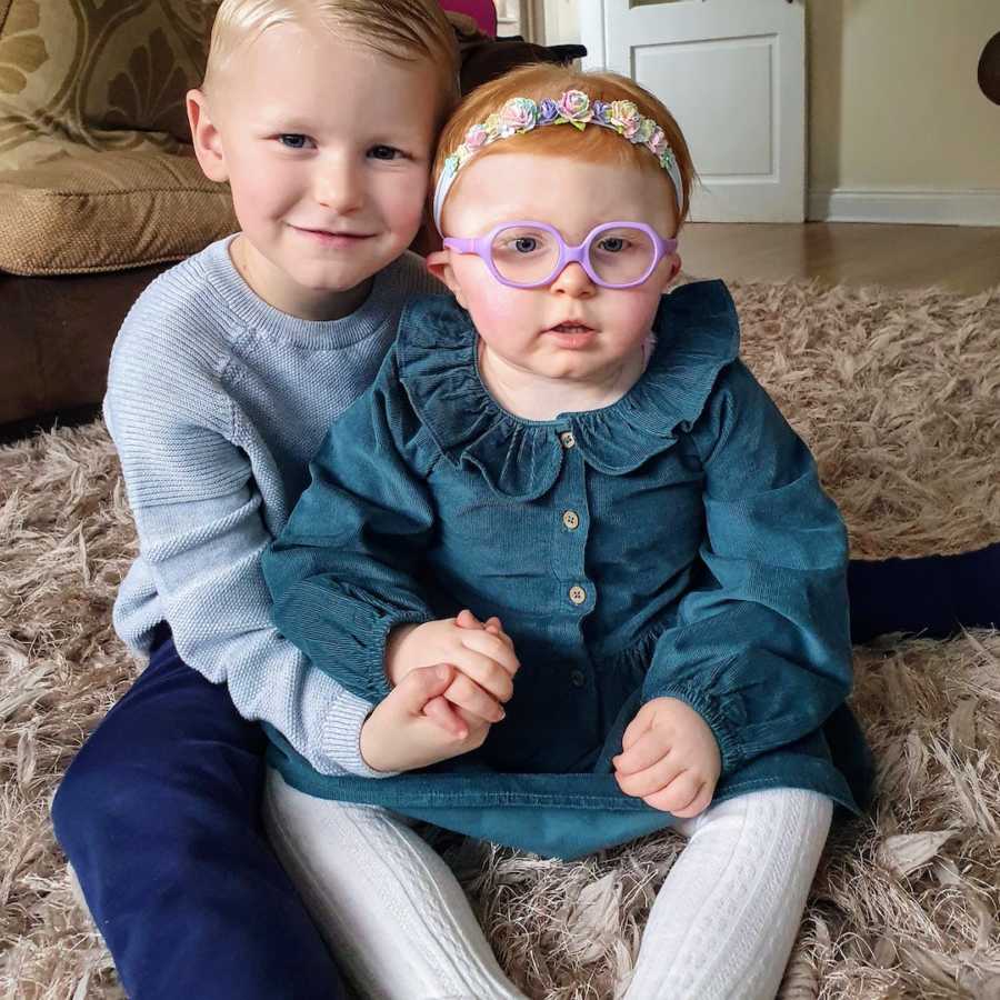 Brother holding baby sister sitting on floor