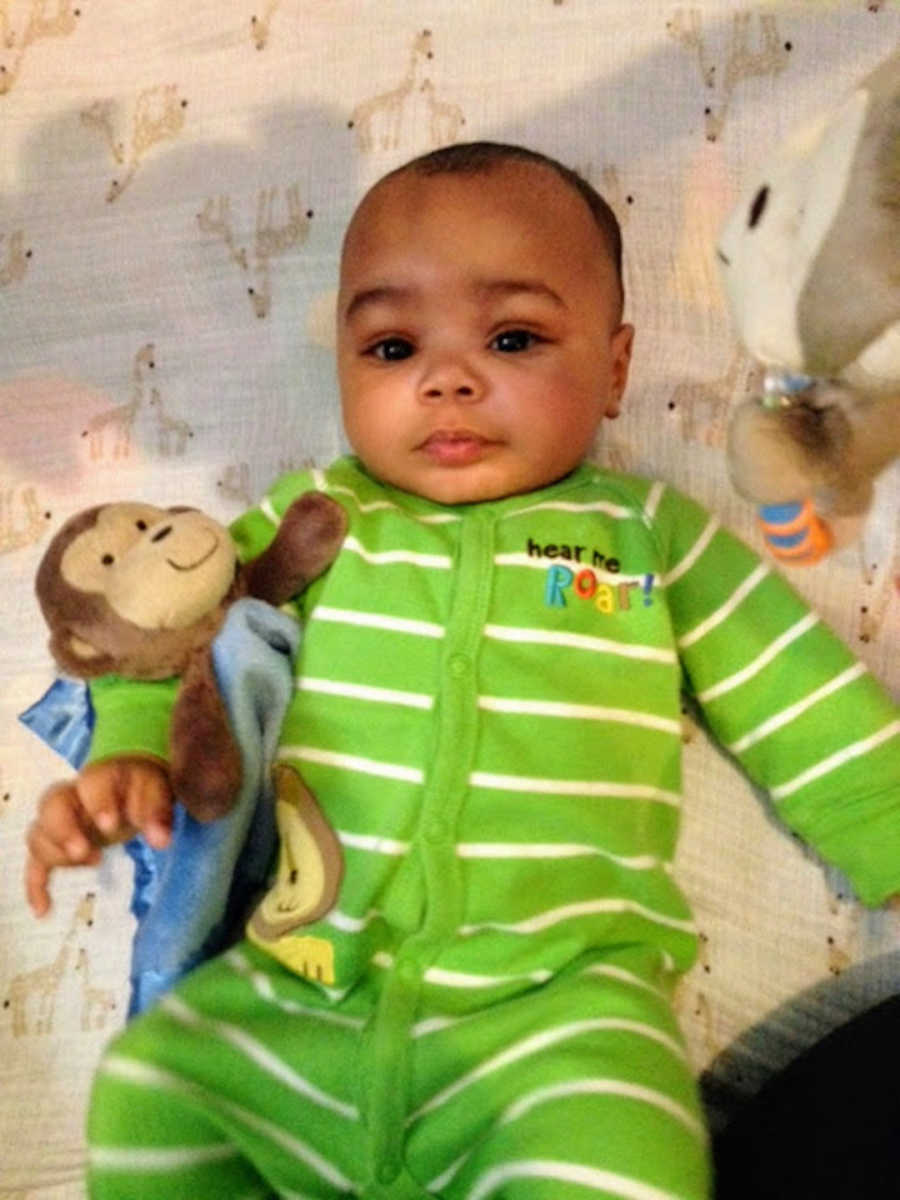 Baby wearing green onesie holding monkey stuffed animal