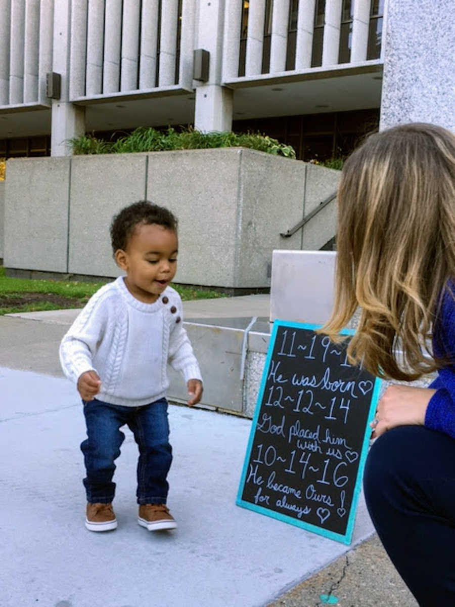 Newly adopted boy standing outside with mom holding chalkboard sign