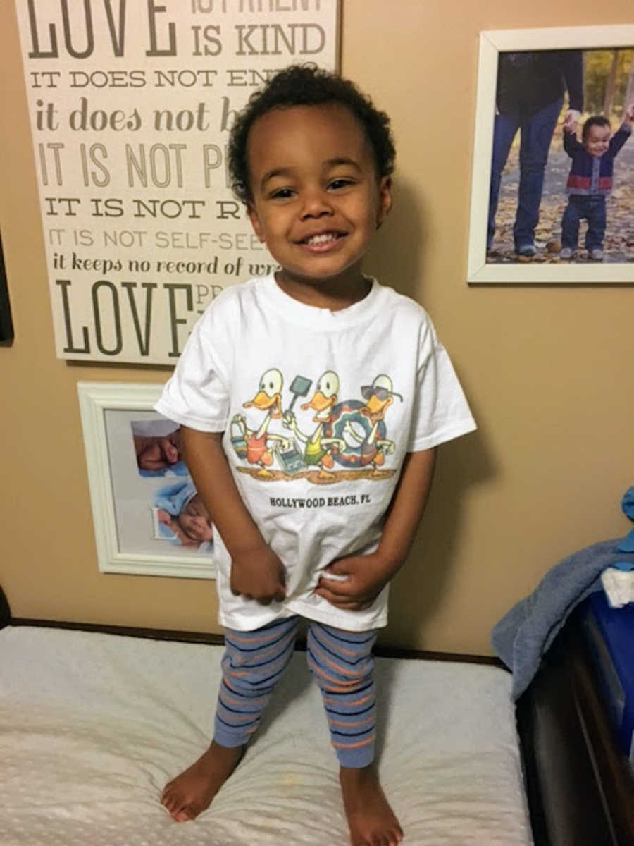 Boy standing in front of wall wearing white shirt and smiling