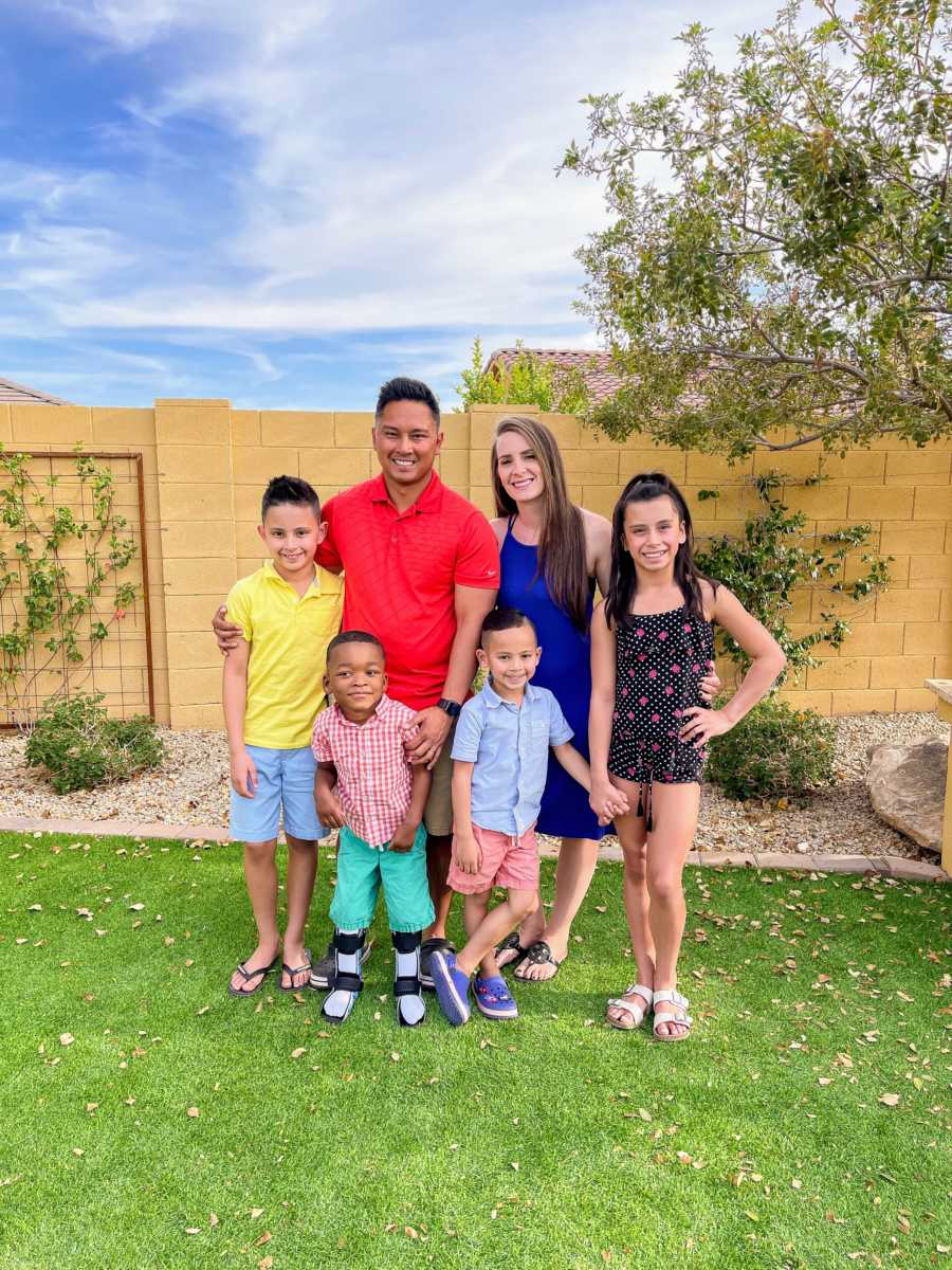 Family of 6 standing in backyard with arms around each other and smiling