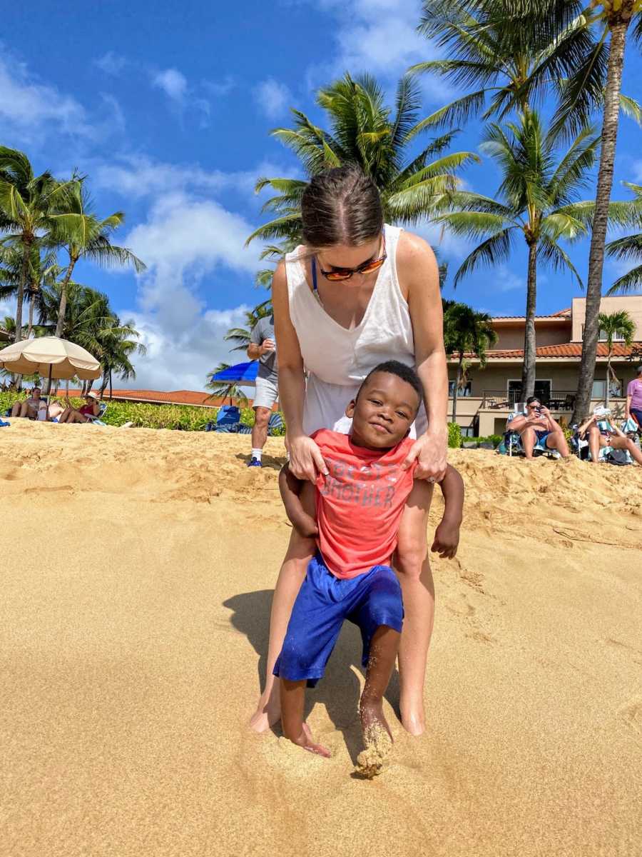 Mom and adoptive son standing together on a beach with palm trees