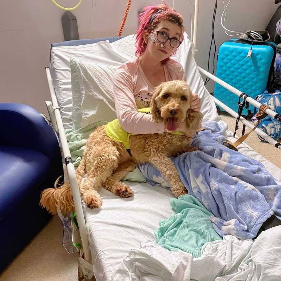 Woman with pink hair holding service dog in inpatient care