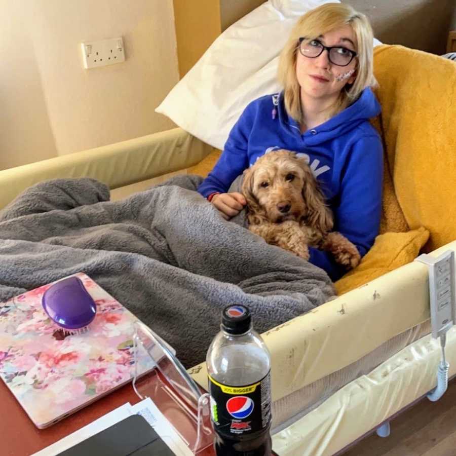 Woman in blue sweatshirt holding Goldendoodle in a hospital bed