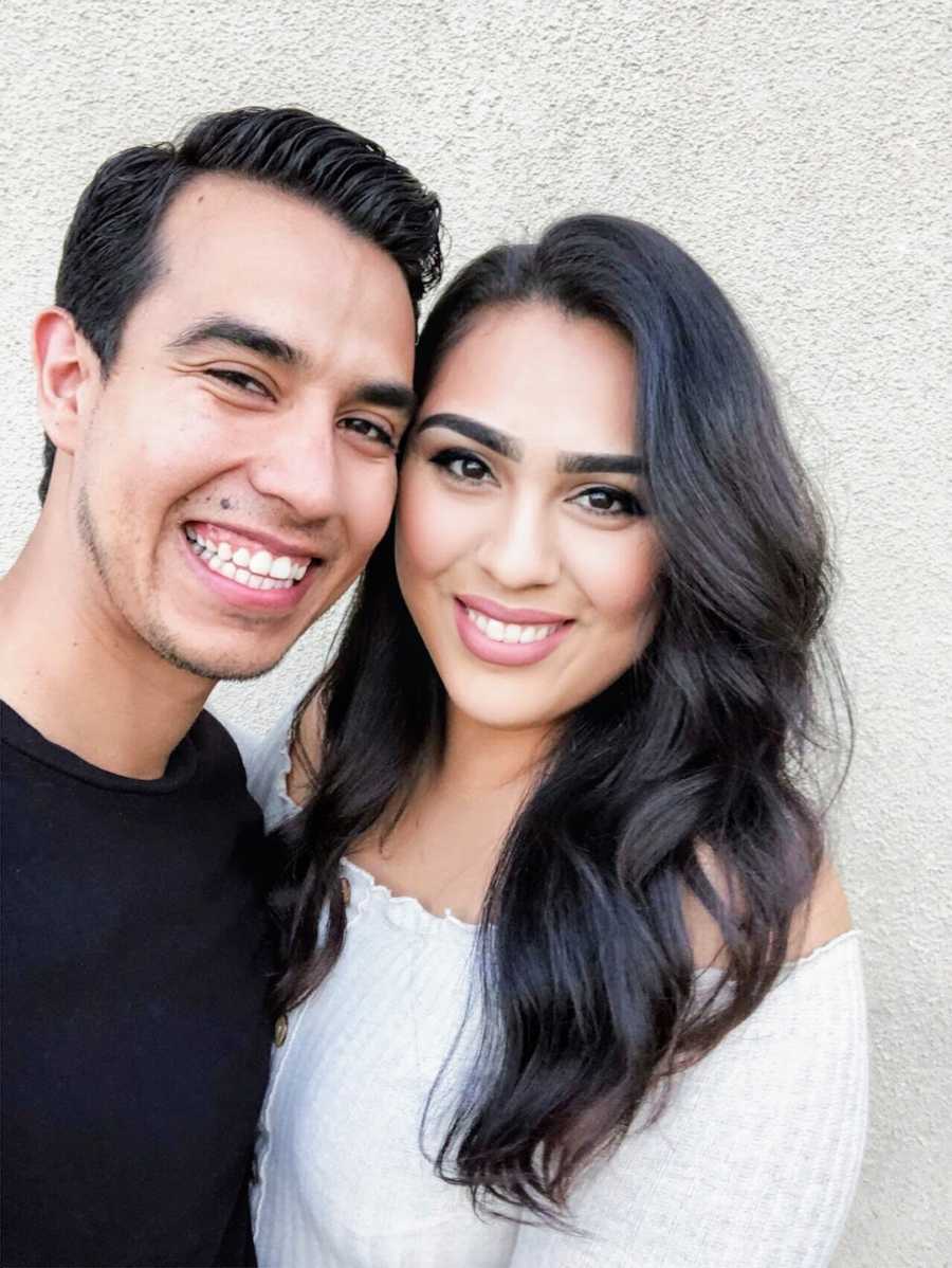 Selfie of a couple smiling in front of white wall