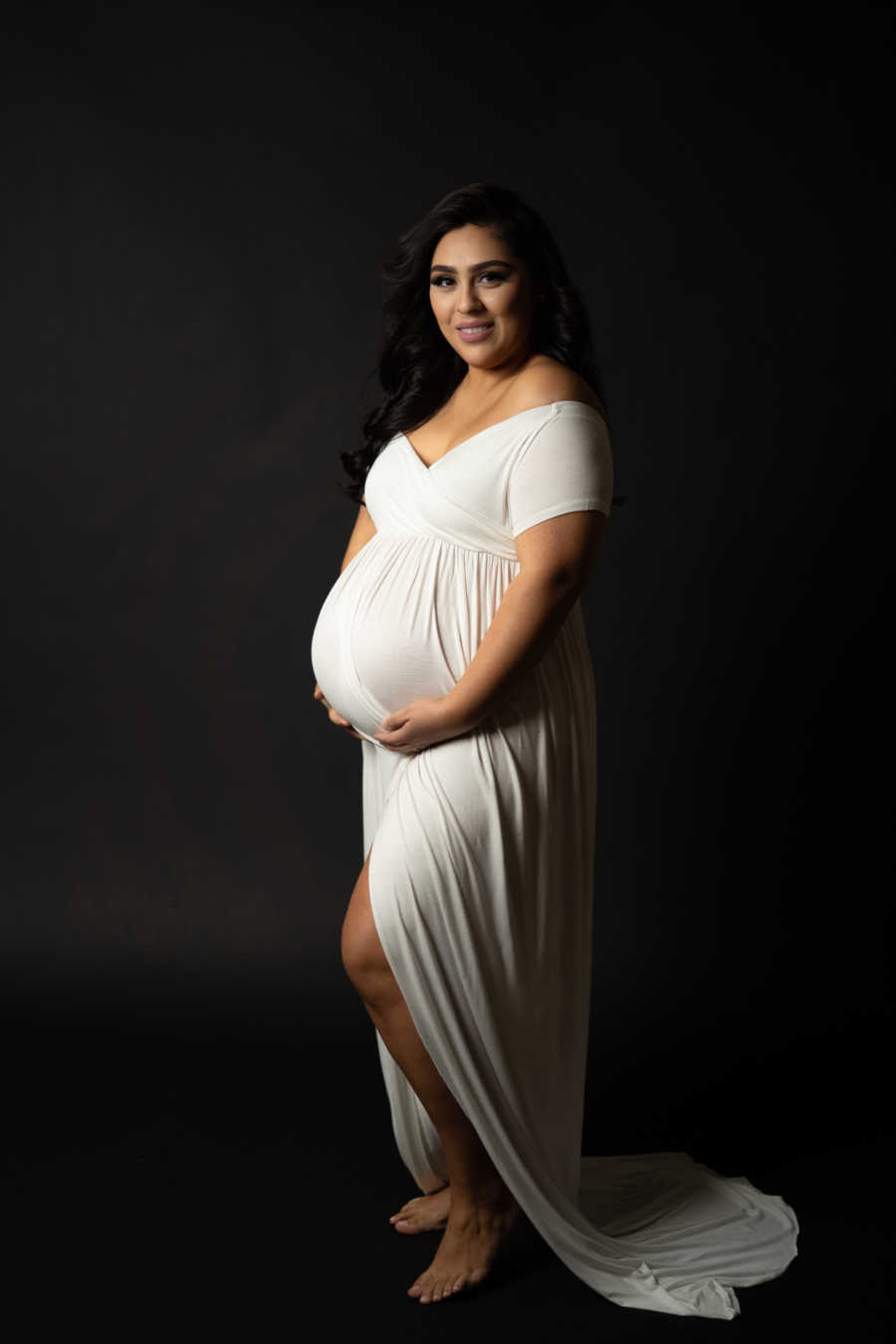 Pregnant woman wearing white dress standing alone