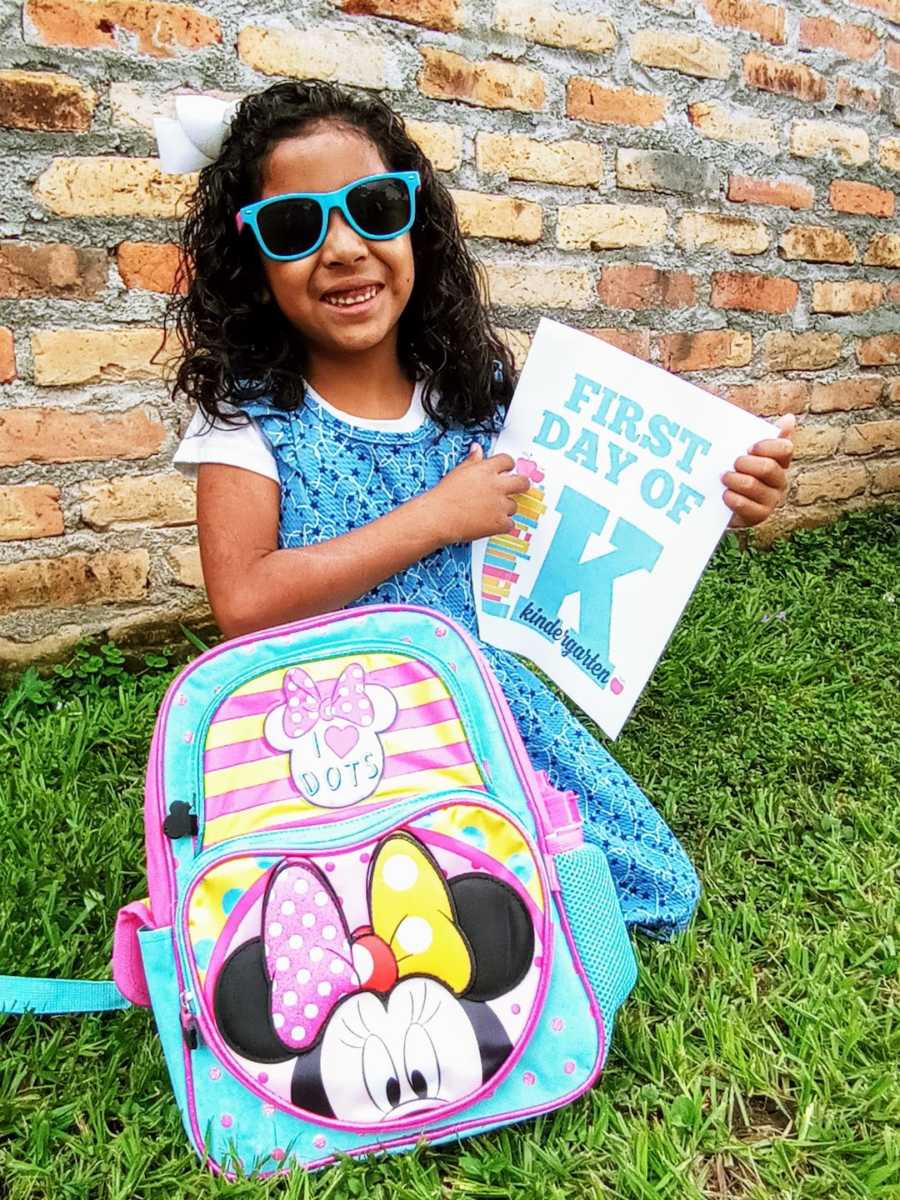 Young girl sitting outside with backpack wearing sunglasses