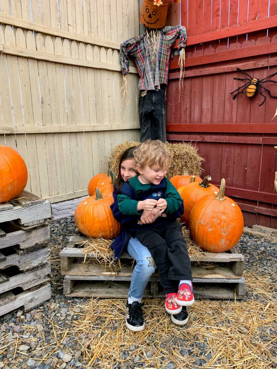 Girl hugs autistic brother on lap near pumpkins