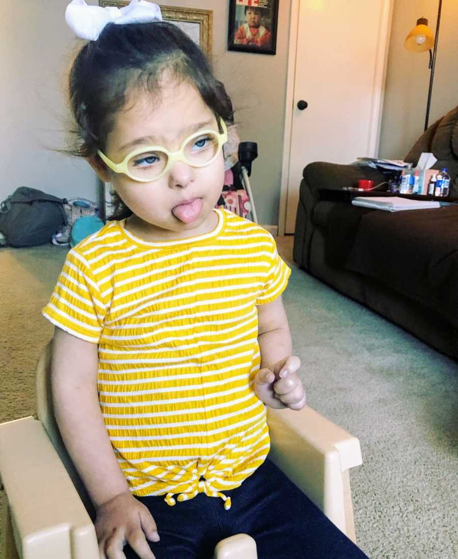 A girl with Down Syndrome wearing glasses sticks her tongue out