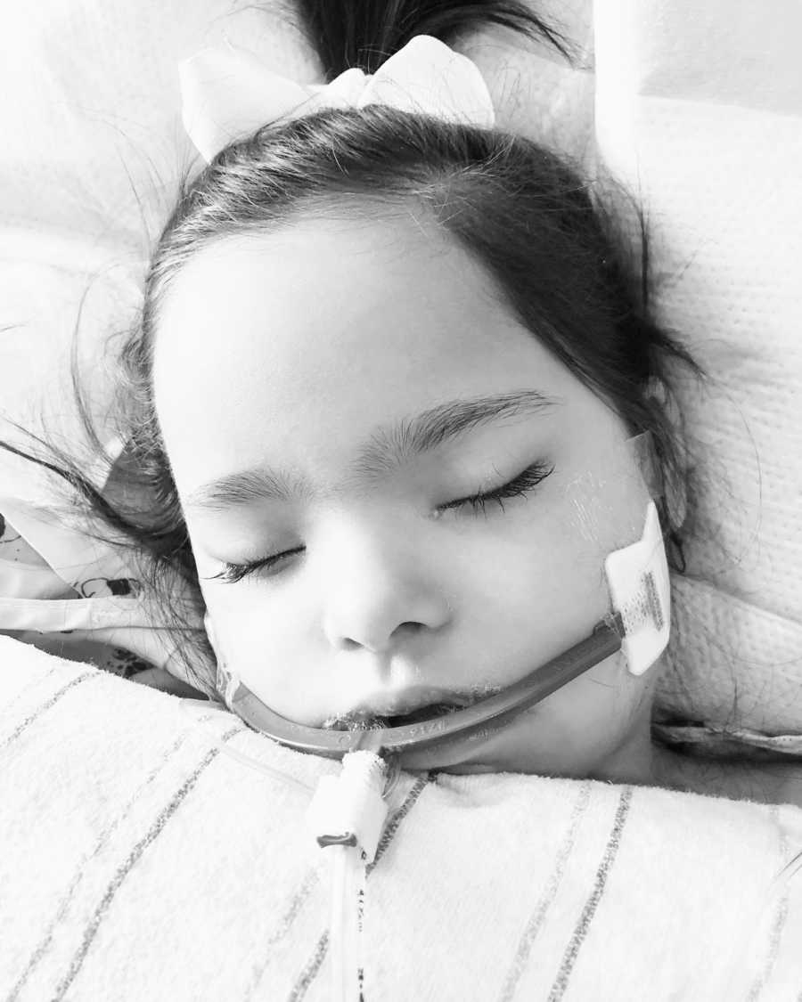 A girl with Down Syndrome lays with a tube in her mouth