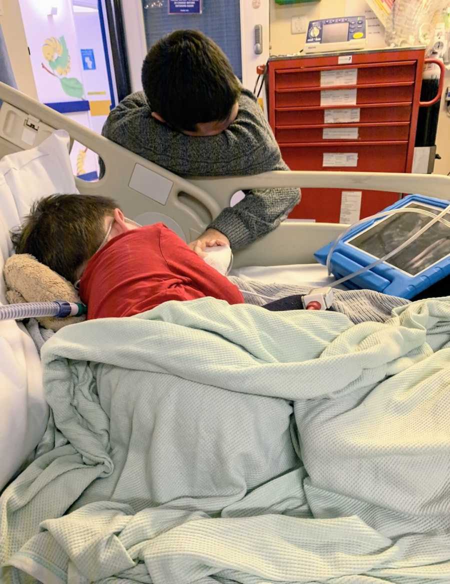 Young boy in hospital bed with tablet and father holding his hand