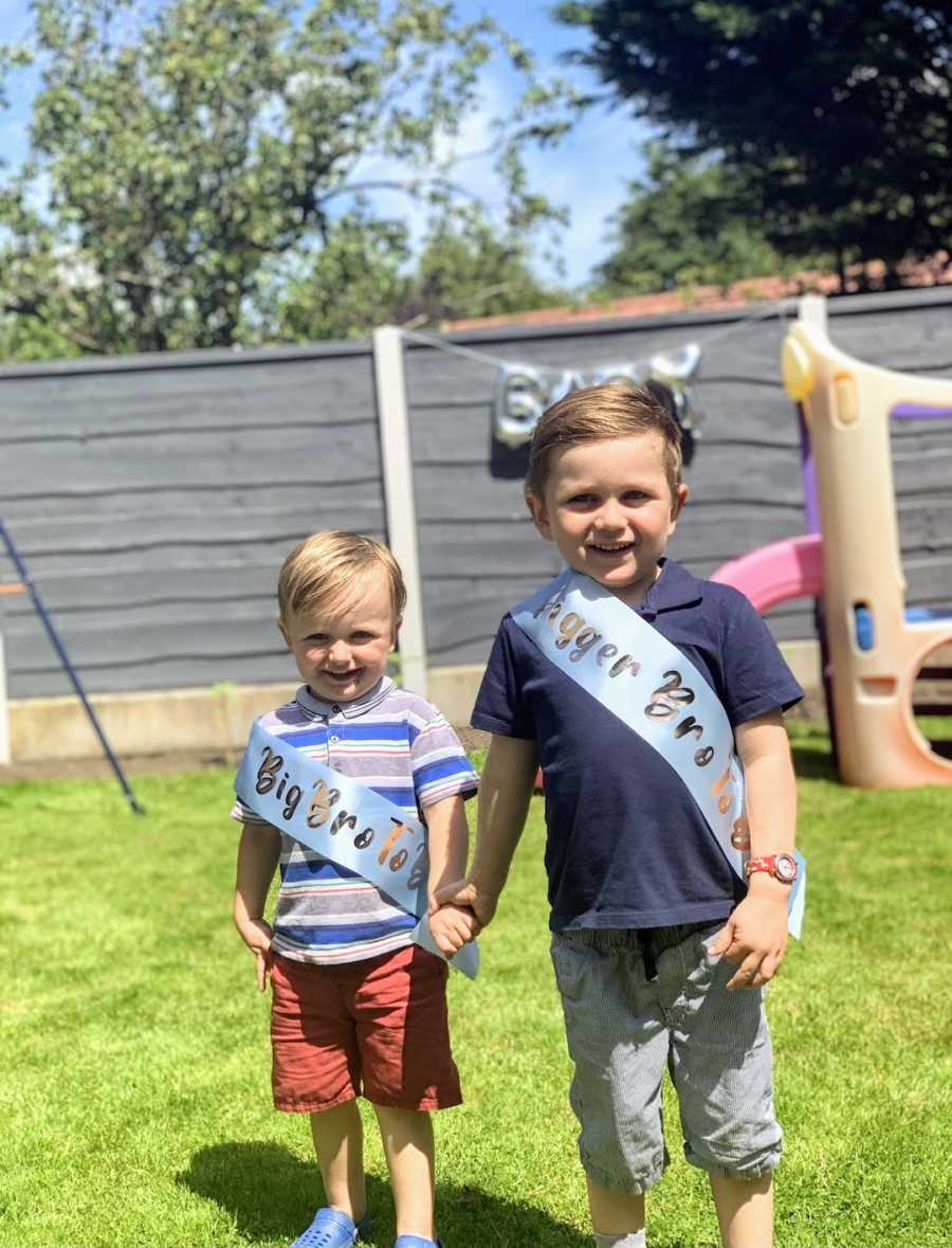 Two brothers holding hands wearing "big brother" sashes