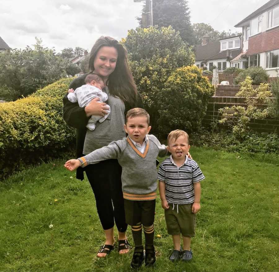 Mother holding newborn daughter standing with two sons in garden