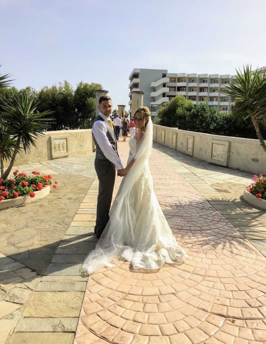 Newlywed couple standing while holding hands and looking at camera