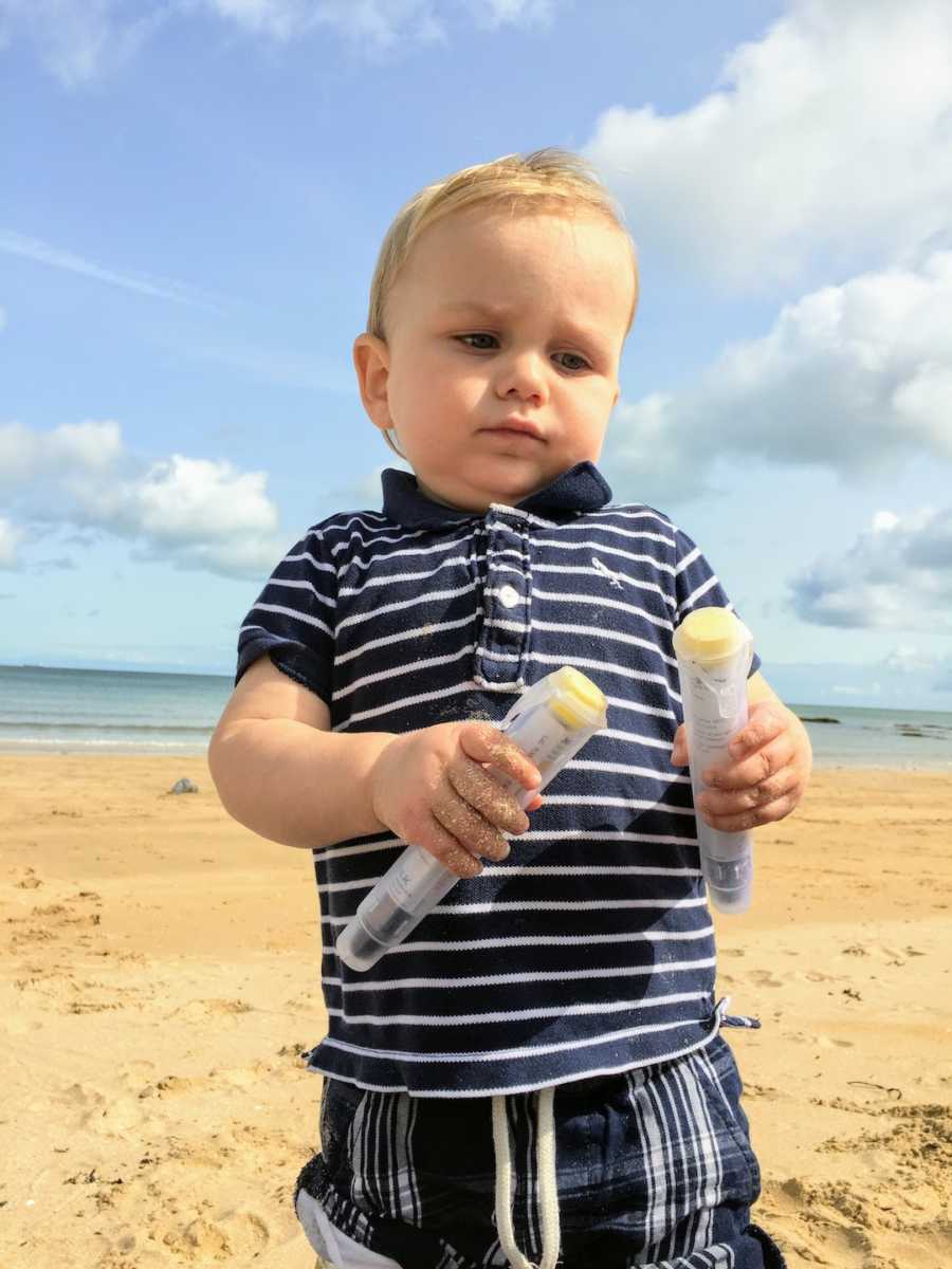 Blonde toddler at beach holding two EpiPens