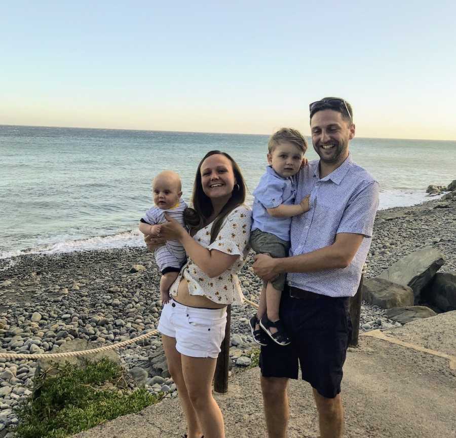 Family of four with two sons standing in front of ocean and smiling