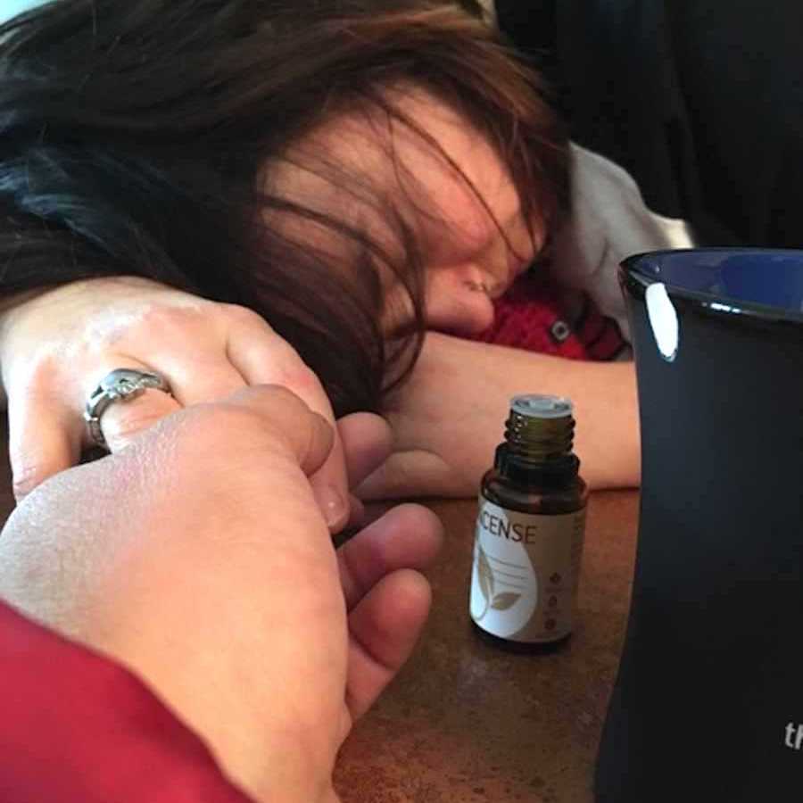 Woman sick with head on table near a bottle of essential oils