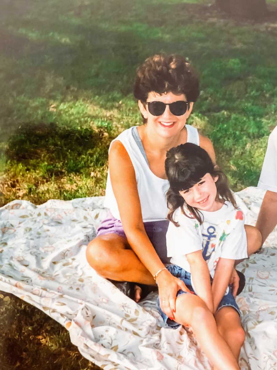 A mother and daughter sit on a picnic blanket on a sunny day