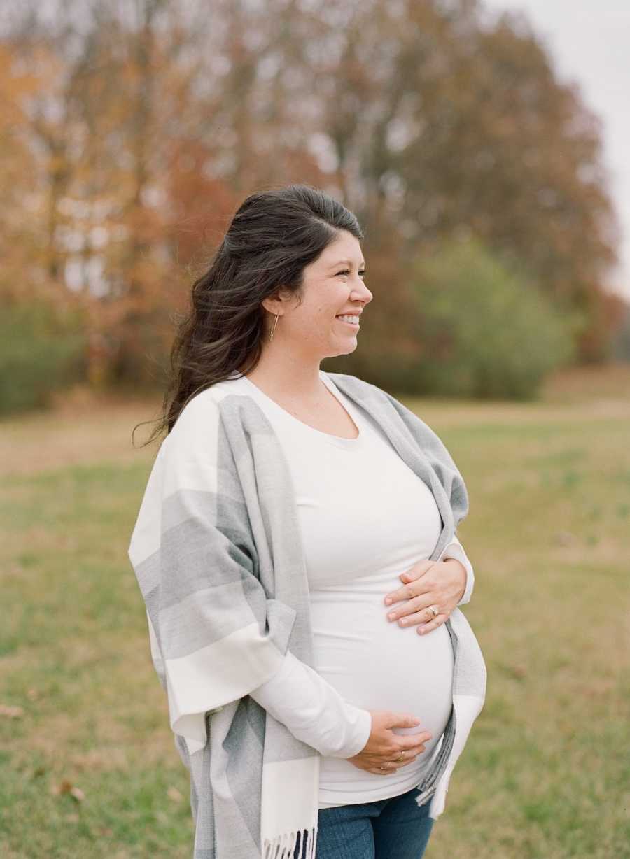 Pregnant woman wearing white holds belly while smiling 