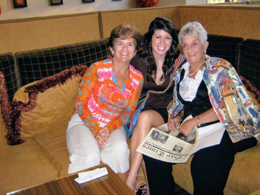 A grandmother, mother, and daughter sit on a couch smiling