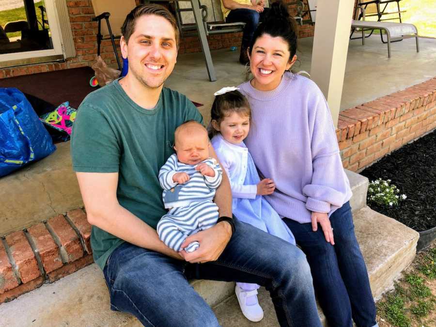 Family of four sitting on front porch steps smiling