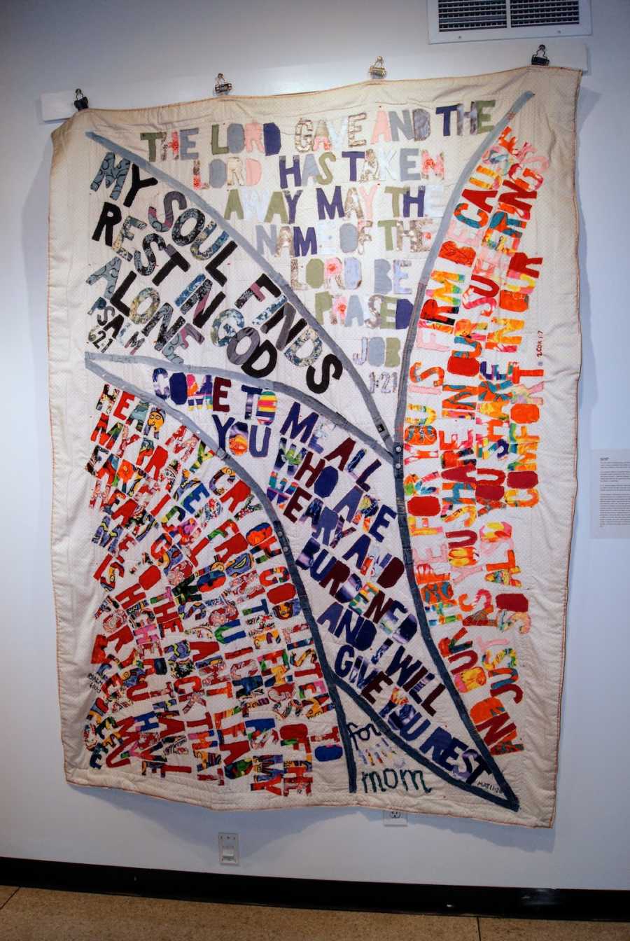 A quilt pinned to a white wall with Bible verses