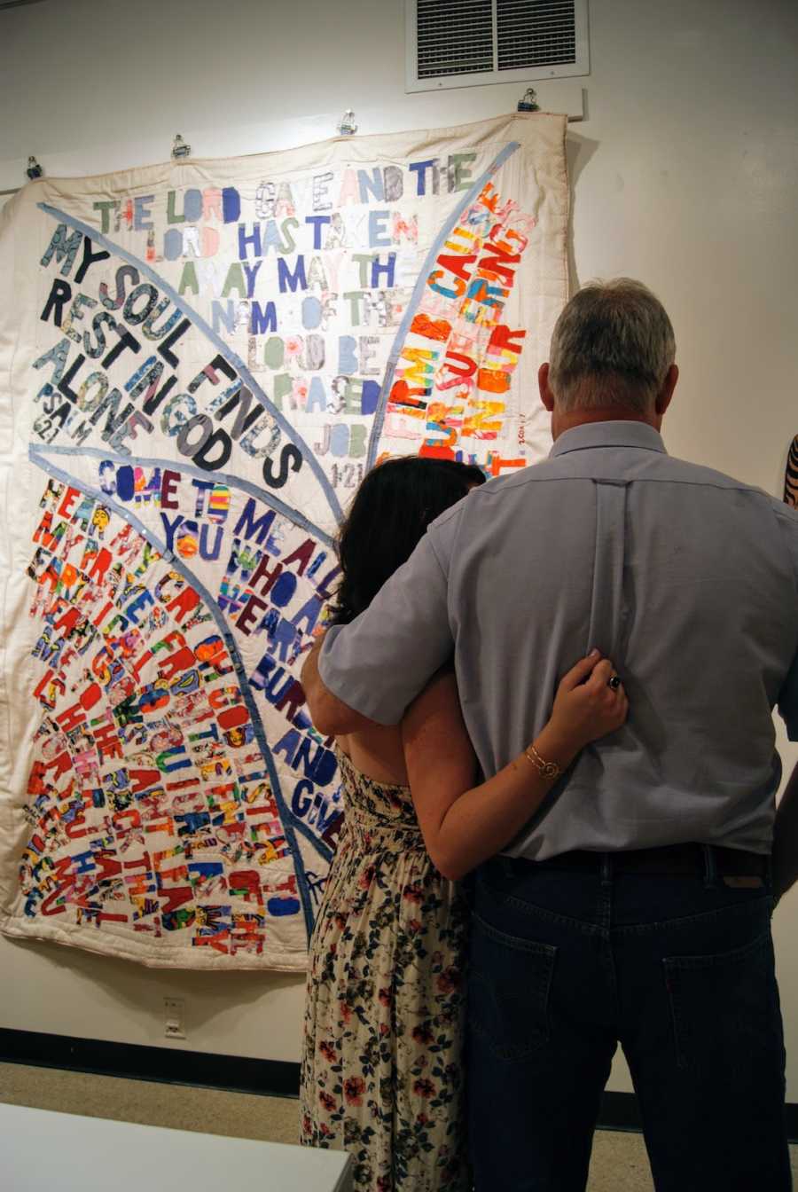 A father and daughter hug in front of a quilt pinned to a wall