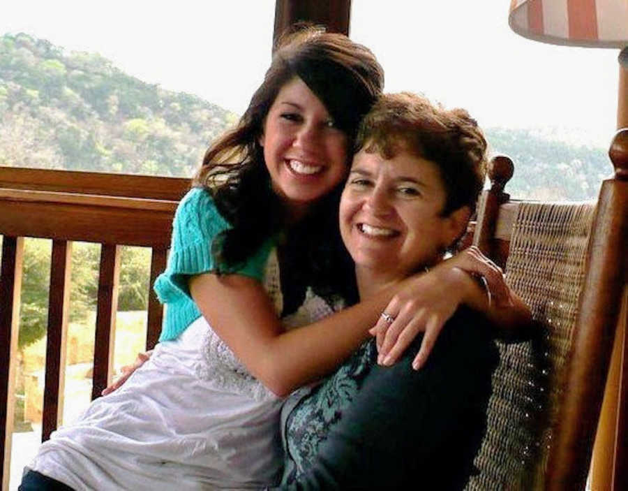 A mother and daughter sit in a rocking chair hugging 