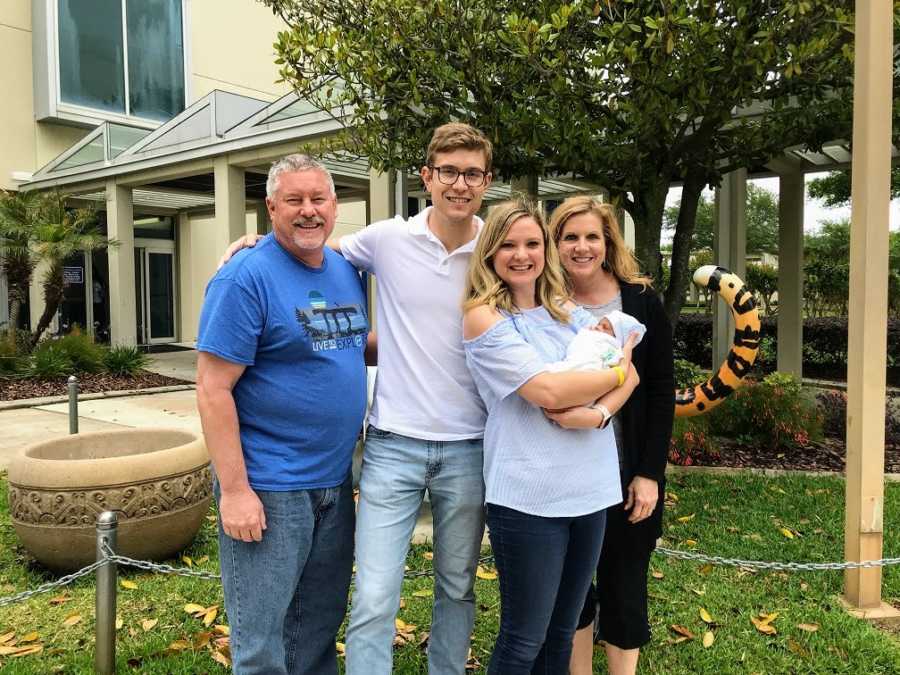 Adoptive parents and in-laws stand together while holding a baby