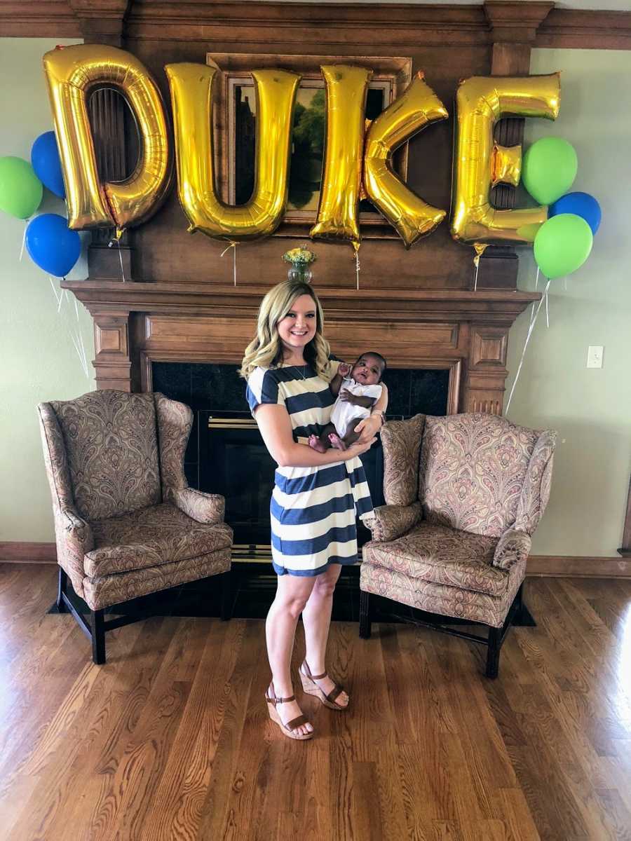 An adoptive mom holds her son in front of balloons spelling his name