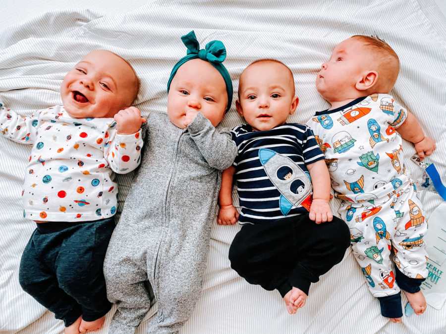 Quadruplet babies lying on a white blanket smiling 