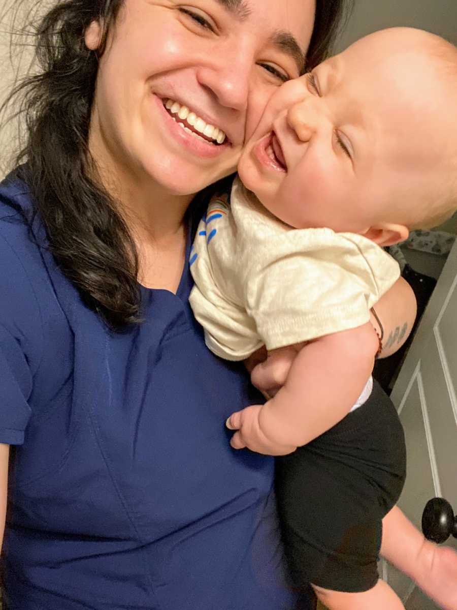 Young mom in blue scrubs holding smiling baby