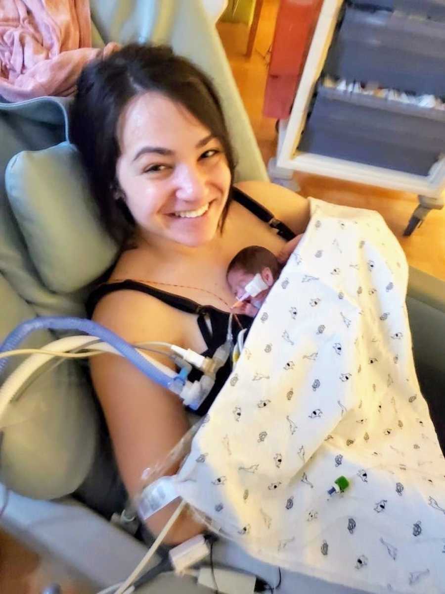 New mom holding premature baby and smiling in a hospital