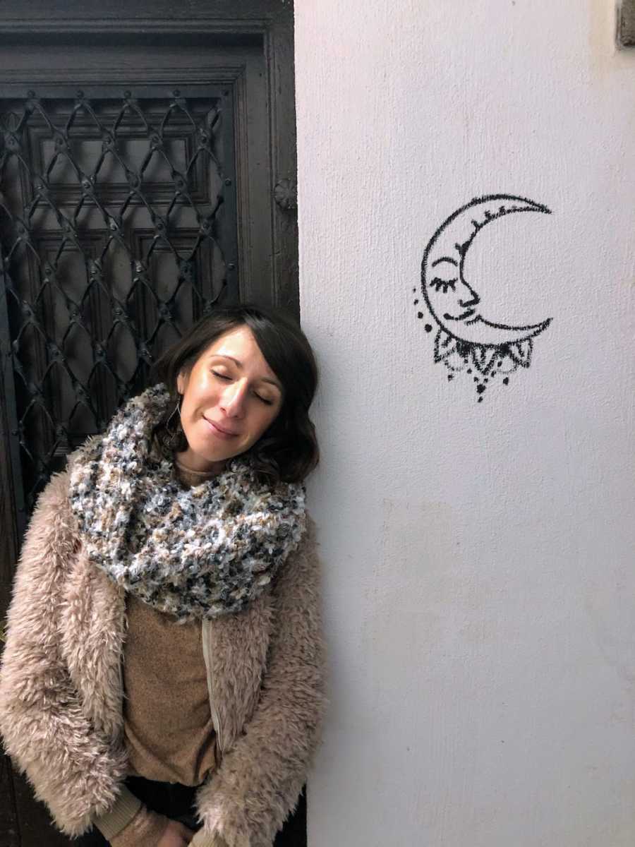 Woman smiling leaning on white wall with moon drawing