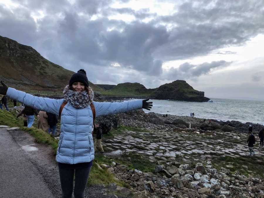 Woman smiling with arms outstretched in front of ocean