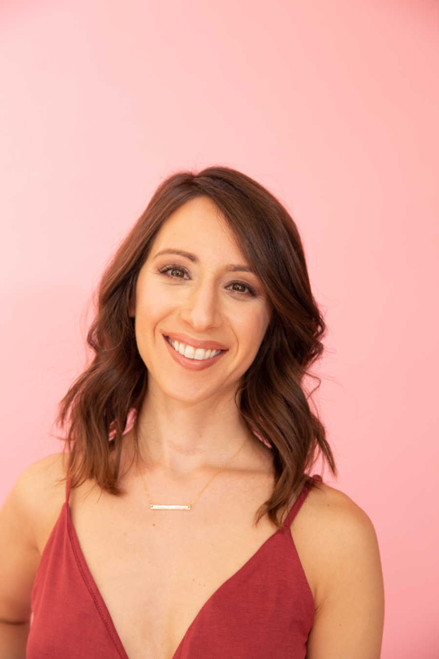 Woman wearing red dress smiling in front of pink background