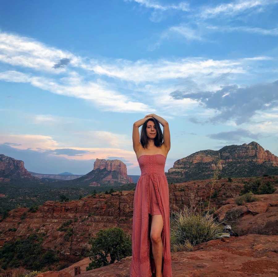 Woman wearing pink dress with arms on head in front of canyon