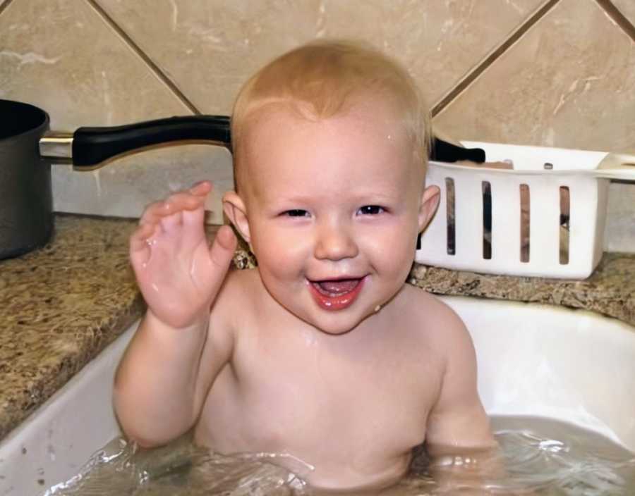 A boy sits shirtless in a sink for a bath