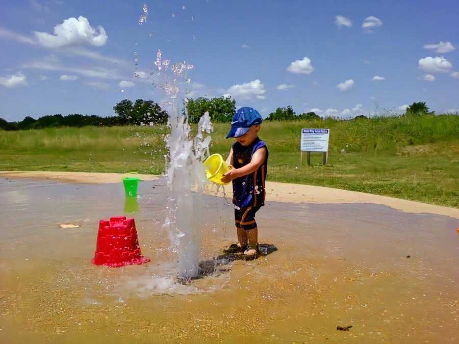 A boy holds a pail near a water fountain