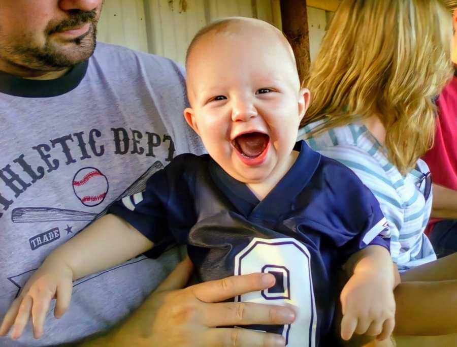 A boy in a jersey sits on a man's lap with his mouth open