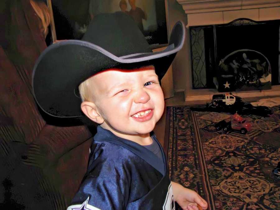 A boy wearing a jersey and a cowboy hat smiles and winks at the camera