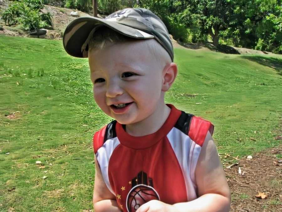 A boy wearing a baseball cap and a red basketball shirt