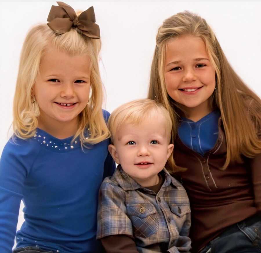 A young boy sits with his older sisters