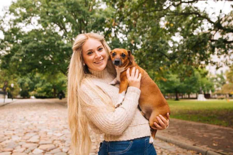 Blonde girl smiling standing outside holding brown weiner dog