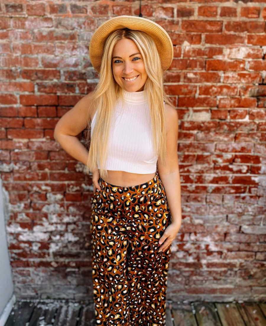 Blonde girl smiling wearing hat standing in front of red brick wall