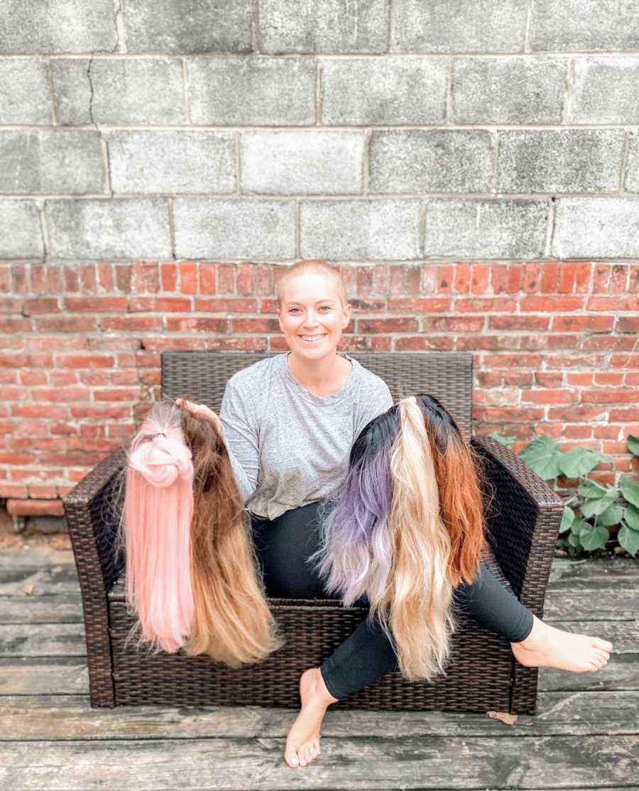 Woman with buzzcut sitting on bench holding wigs